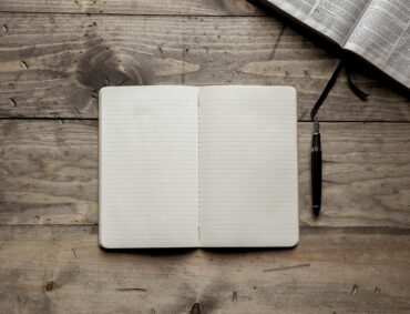 Illustrative open journal and Bible on a wooden table.